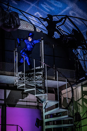 A person dressed in a blue suit on top of some stairs in a theatrical setting.