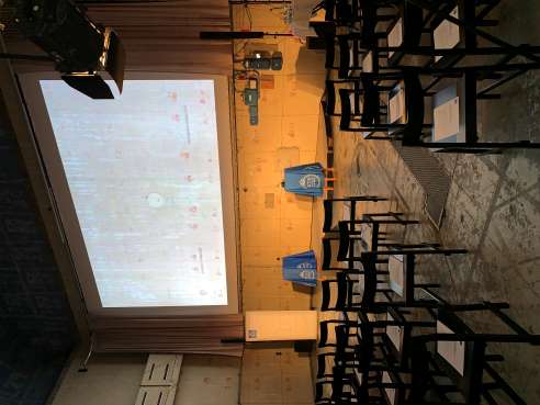 A projector screen and chaits in several rows in front of screen.
