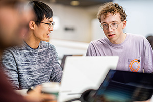 Two students sitting talking with each other. Laptop in foreground.
