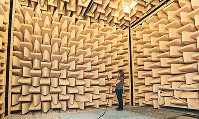 A woman with a sound instrument standing in a room covered in noise-reducing material.