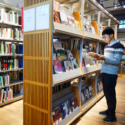 Doctoral student standing in front of a shelf with journals, reading in a journal