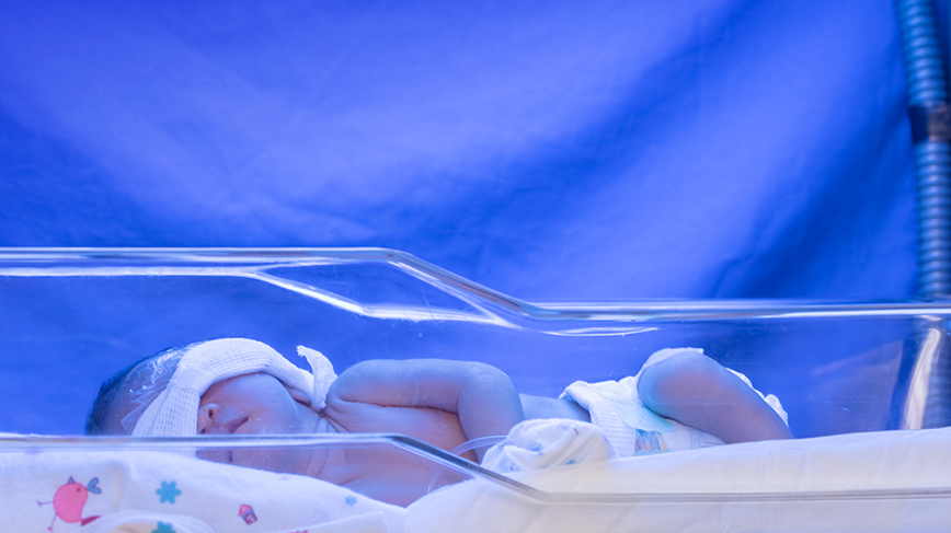 Spädbarn i kuvös med blått ljus