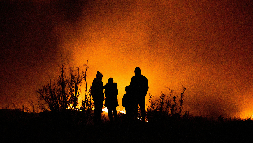 Siluetter av människor som betraktar en skogs/markbrand.