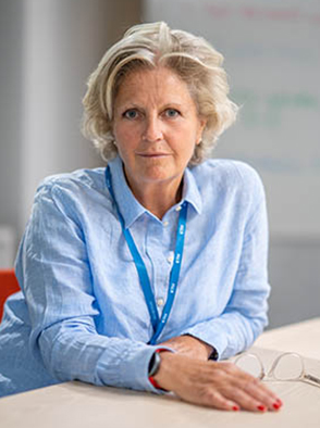 A blond woman wearing a light blue shirt sitting behind a table.