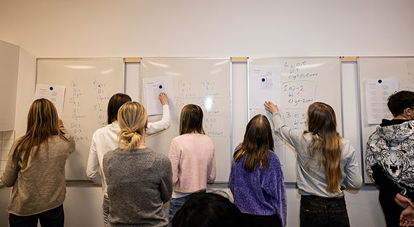 Flera studenter bakifrån som skriva på ett whiteboard