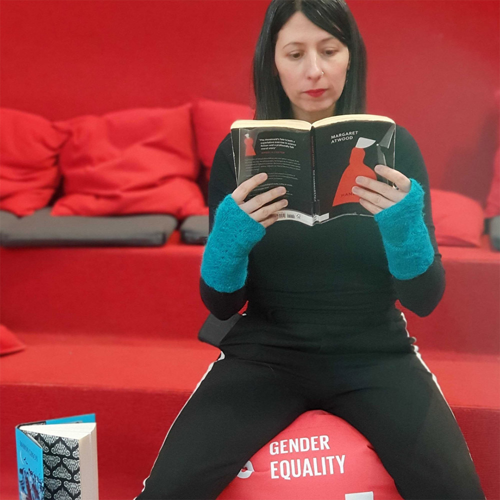 Librarian sitting on a pillow with the text gender equality reading a book.