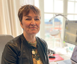 En leende kvinna i kort brunt hår vid ett skrivbord.