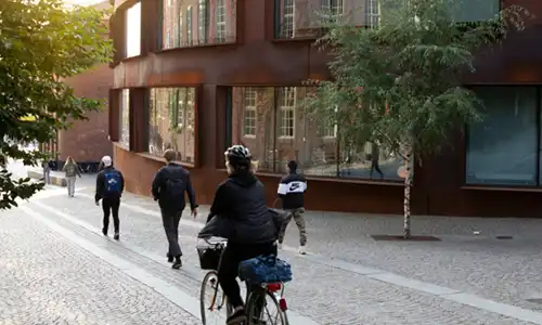 Gående personer och en person på cykel framför en byggnad.