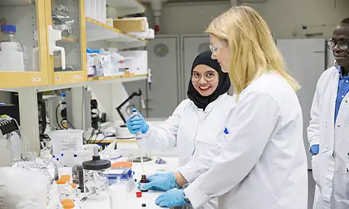Tre personer med labbrockar i ett laboratorie.