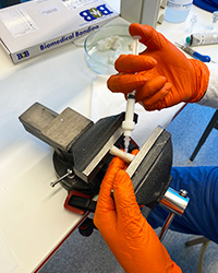 Närbild på händer som applicerar Biomedical Bondings benlim på en benbit i ett skruvstäd.