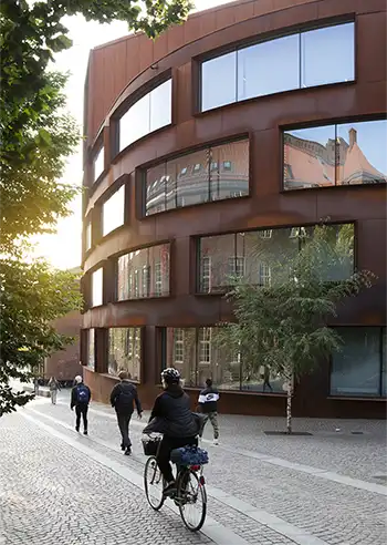 Person on a bike and walking persons in front of a brown buildning.