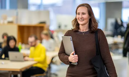 En yrkesverksam student går i Arkitekthuset på KTH och bär på en laptop.