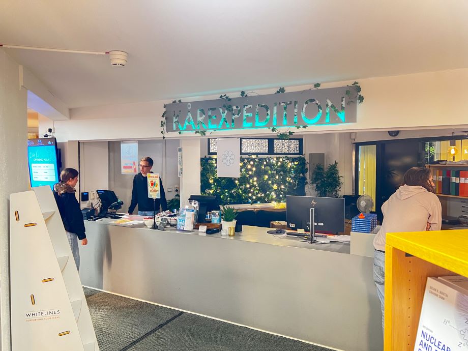 Reception area at THS student union bookstore with 'KÅREXPEDITION' neon sign and staff at counter.