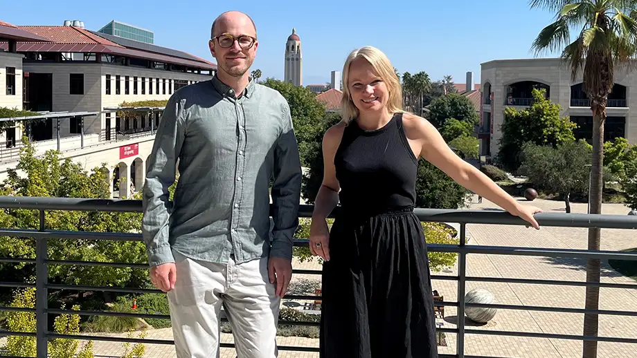 Two people posing on a balcony with Stanford U. campus in background
