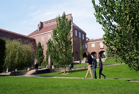 People walking on a lawn in front of a brick builiding.