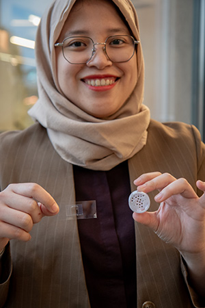 Jessika Jessika håller upp en 3D-printad förstorad modell av sin mikrostruktur och en glasplatta.