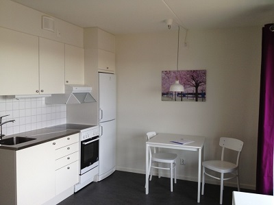 Kitchen along wall facing window with oven, stove, fridge, table and two chairs.