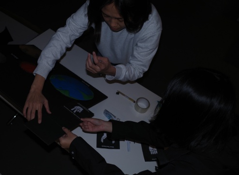 Overhead view of Ke and Tong leaning over a table, working on a cardboard display
