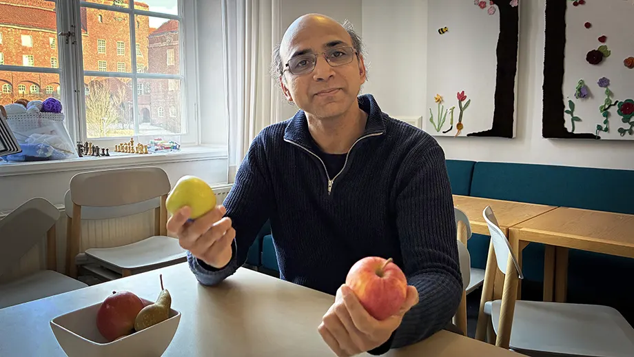 Man sitting at table with green apple in one hand, a red one in the other