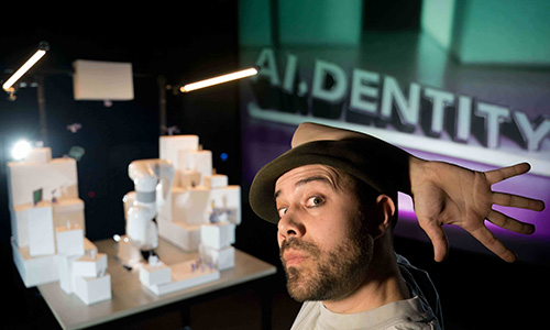 Erik Rosales of AI.DENTITY makes a hand gesture in front of a scale model.