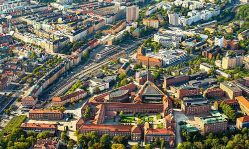 Aerial view of the KTH campus at Valhallavägen, with the red-brick main building surrounded by greenery.