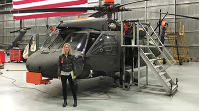 Foto: kvinnlig KTH-praktikant på NASA framför helikopter i hangar med amerikanska flaggan bakom.