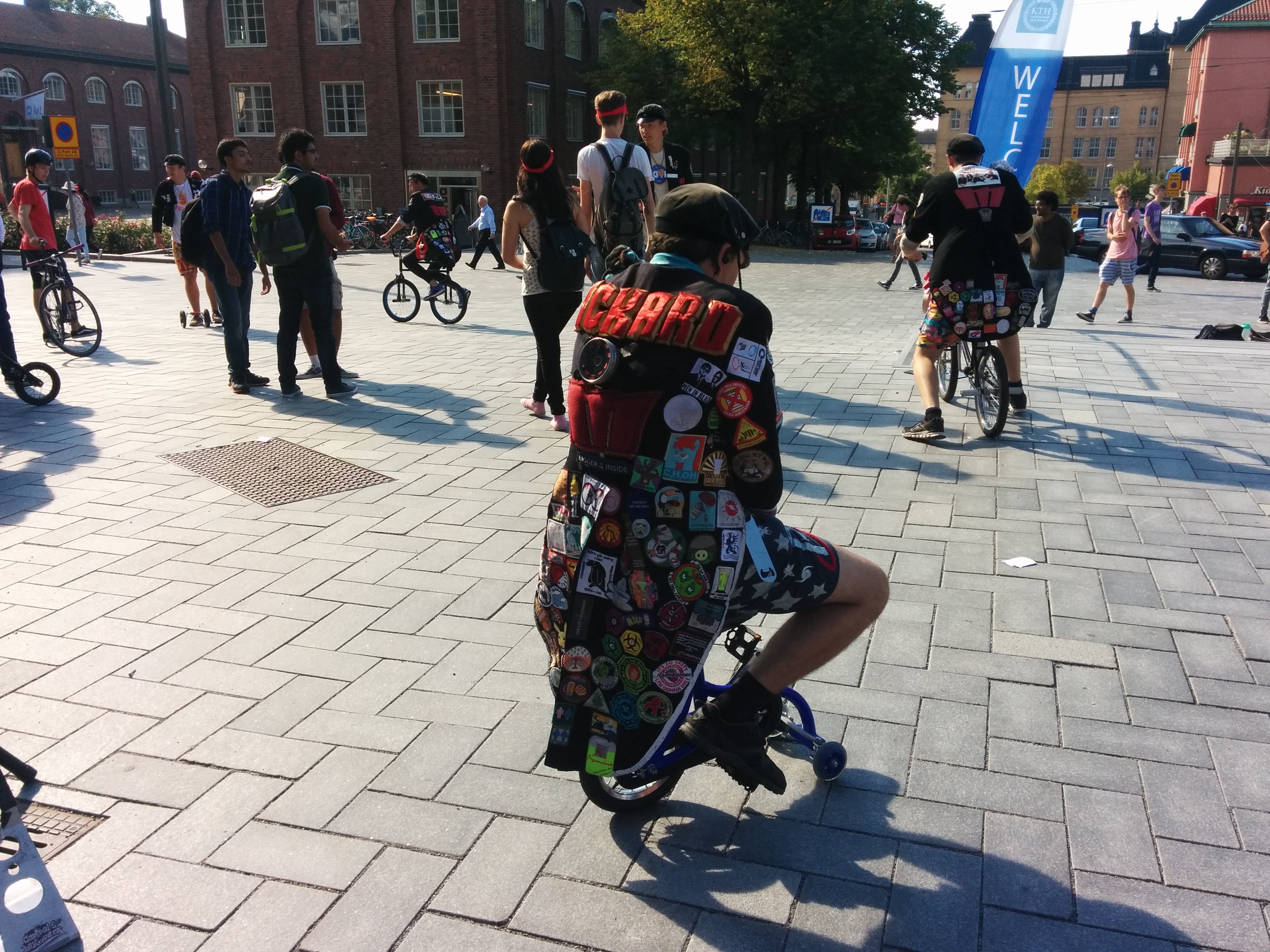 Student cyklar på minicykel iförd studentikos frack med märken