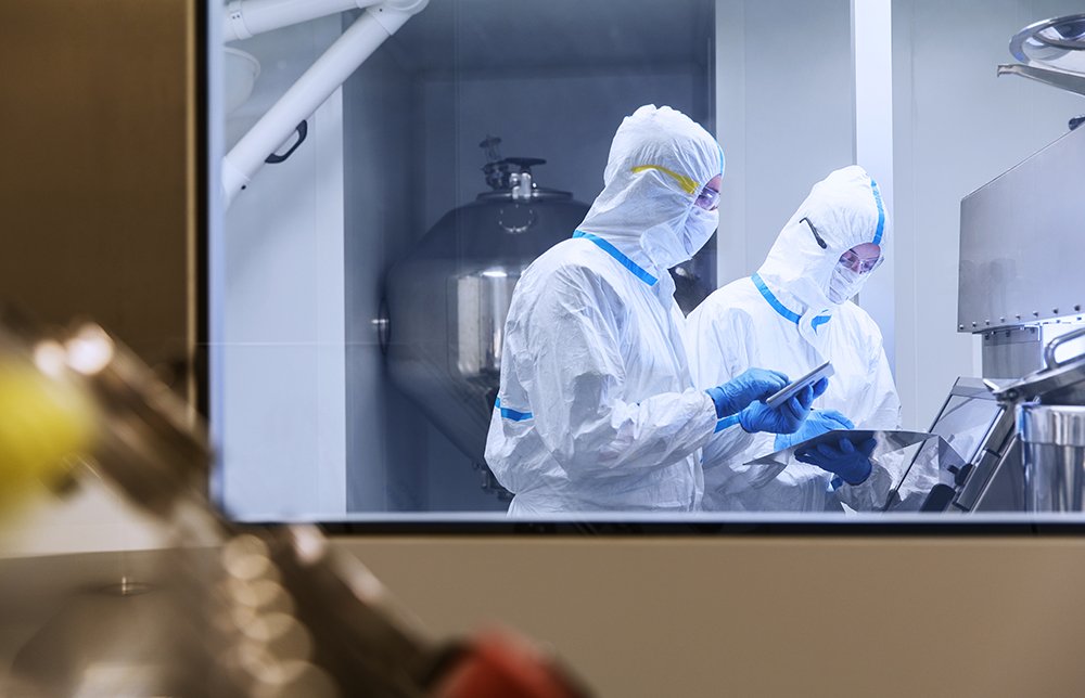 Två forskare iklädda skyddsdräkter står i ett labb och arbetar.