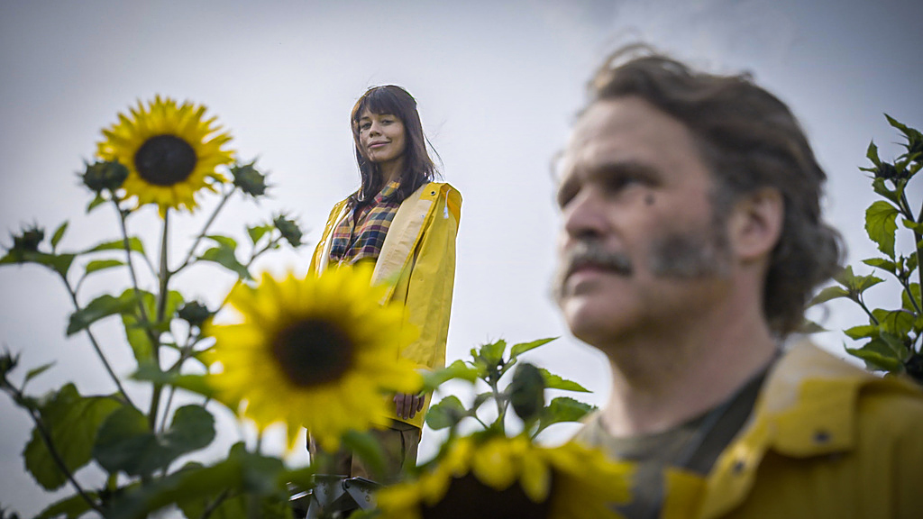 TV-personligheterna Lotta Lundgren och Erik Haag som står och sitter på ett fält fullt av blommor. Kamerans fokus är på Lotta.