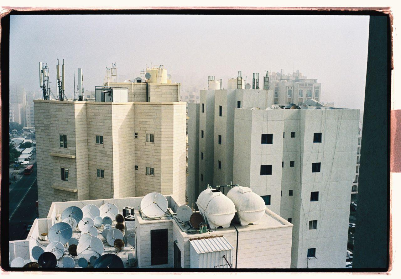 Bild av några flerfamiljshus i en stad. Ett antal parabolantenner återfinns på ett av hustaket, på ett annat återfinns mobilmaster.
