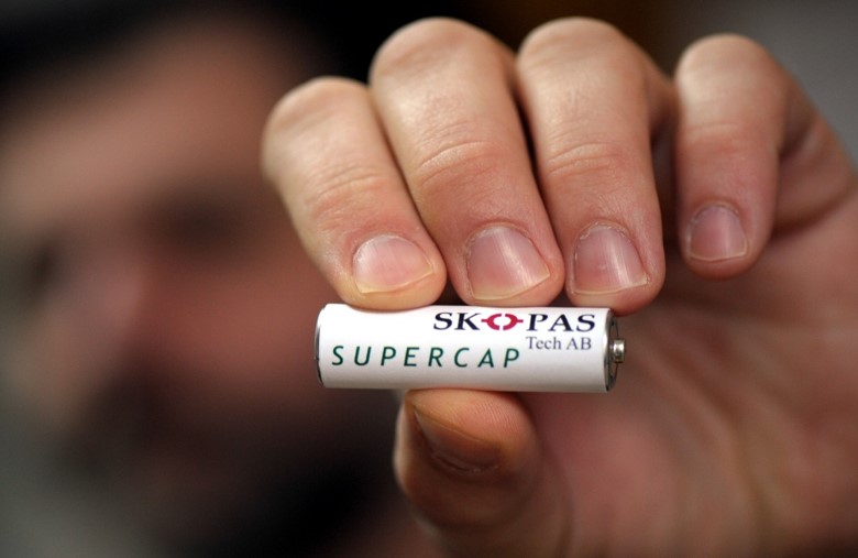 A hand holding up a battery with SKOPAS written on the side.