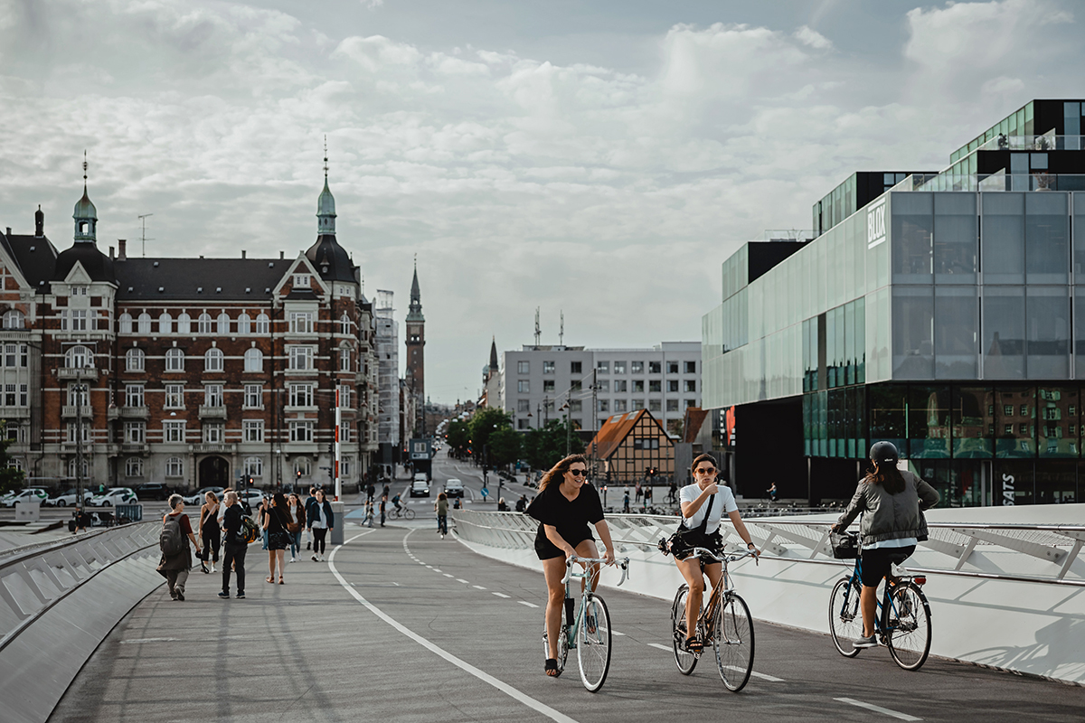Fotografi visar en stad med en cykelbana. I förgrunden tre cyklister och längre bak ett antal gångtrafikanter.