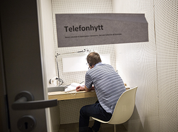 En man sitter på en stol i en hytt och pratar i telefon.