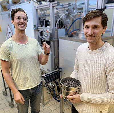 Två personer, forskarna Joar Huss och Johan Martinsson, ståendes i ett labb på KTH, en testugn, visar upp järnsvamp som är en form av järnmalm.