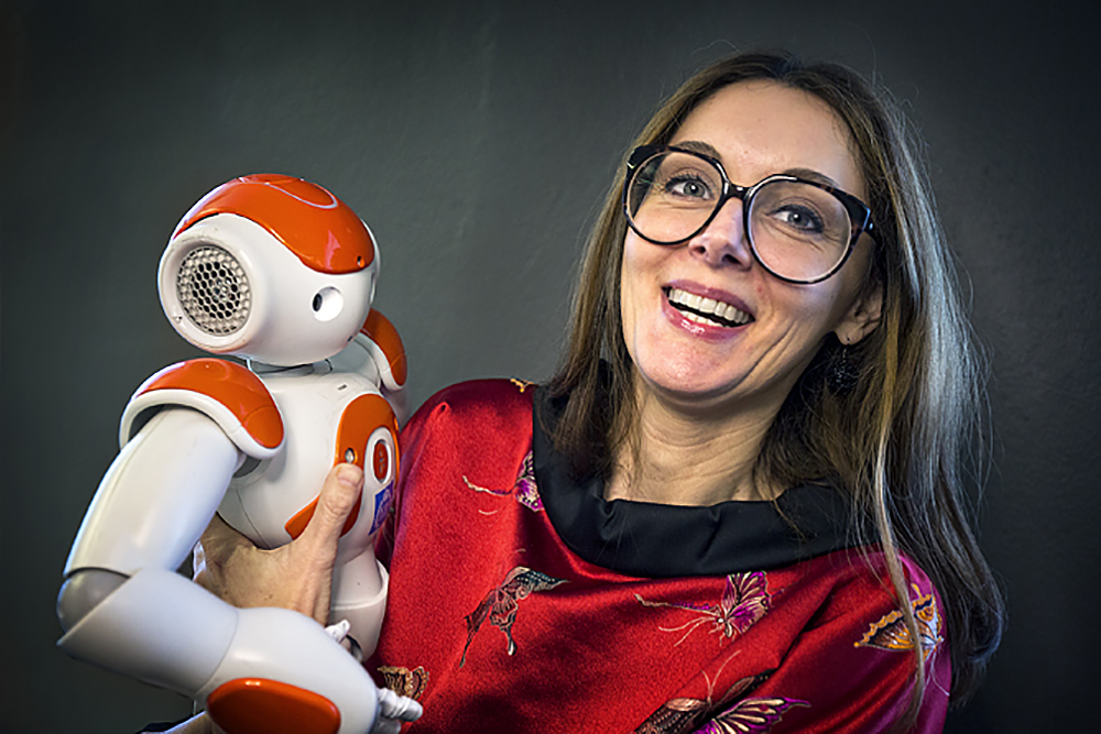 Danica Kragic Jensfelt, professor i datalogi, håller en robot i famnen. Hon ler stort. 