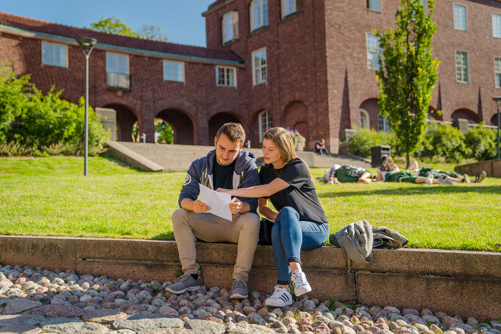 Ett par studenter - en tjej och en kille - sitter ner på borggården på KTH:s campus på Valhallavägen