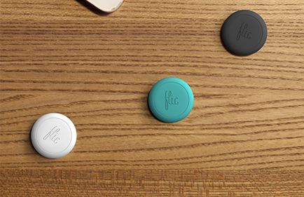 Tre flic-knappar som ligger på ett träbord. Knapparna är runda, ca. 3 cm i diameter och i färgerna vitt, turkost och svart. 