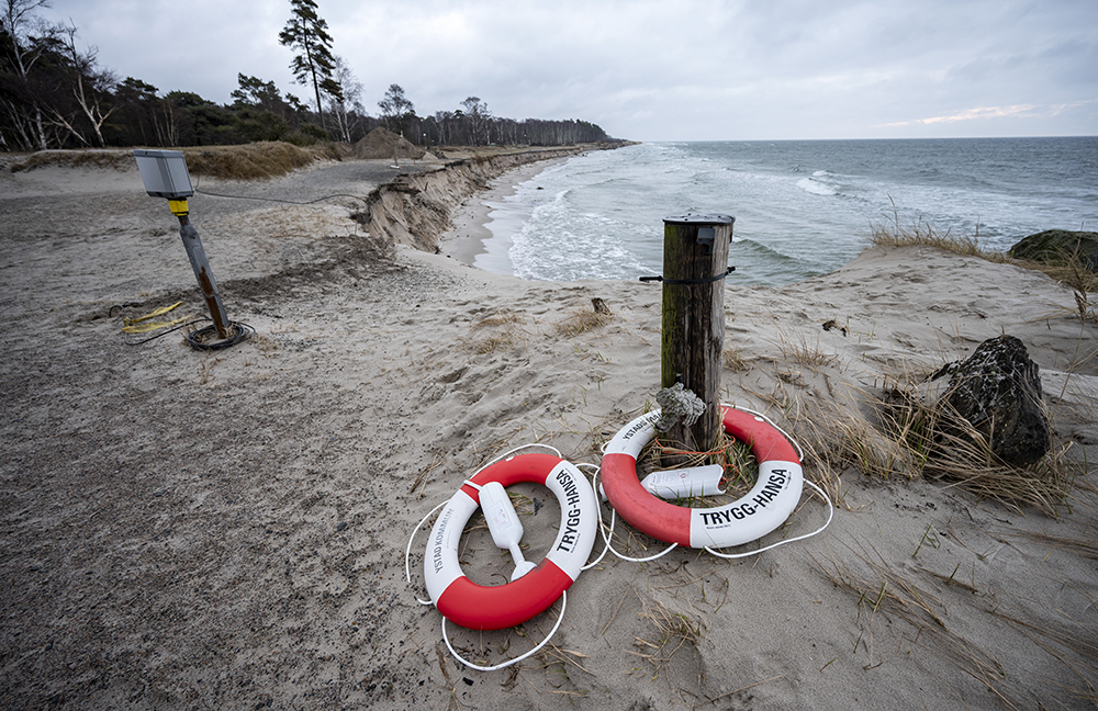 Vågor slår in mot en sandstrand vid Löderup, på skånska sydkusten. I förgrunden ligger två livbojar på strandkanten. 